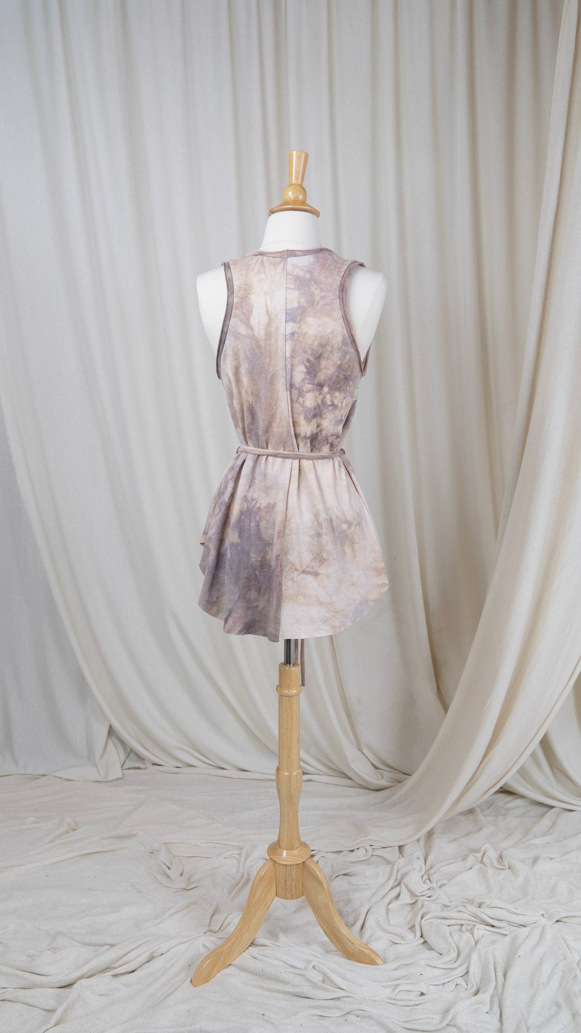 one light rose colored tank top with a scoop neck and a belted waist hangs from a bust with the back facing the camera.