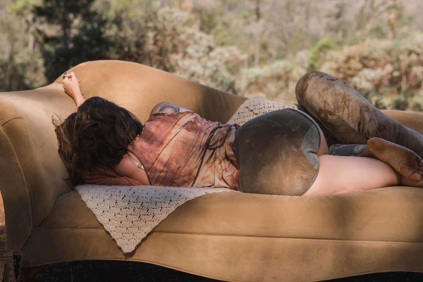 One model wears a cropped tank top in earth toned underwear outside with a couch and green trees