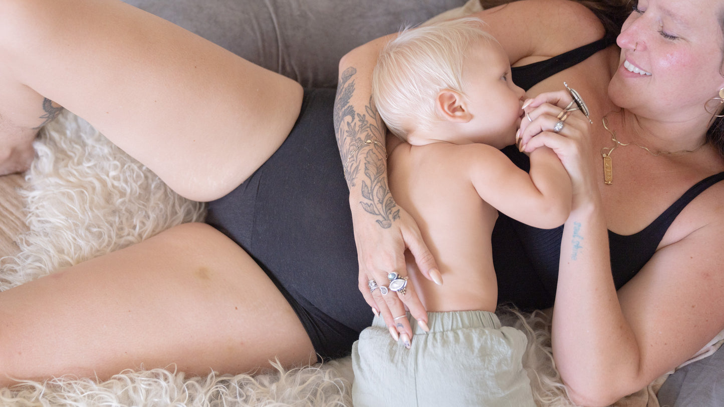 smiling woman holding baby wearing black bra and period underwear