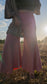 close up of woman standing in sun-lit field with trees in background wearing stretchy, peachy-pink, high-waisted, flowing, gaucho pants