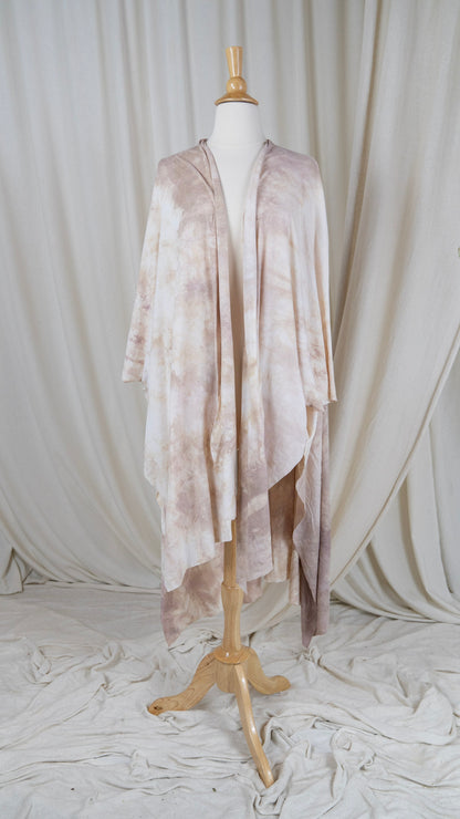 One light pink and white shawl hangs from a bust in front of a white curtain with the front facing the camera.