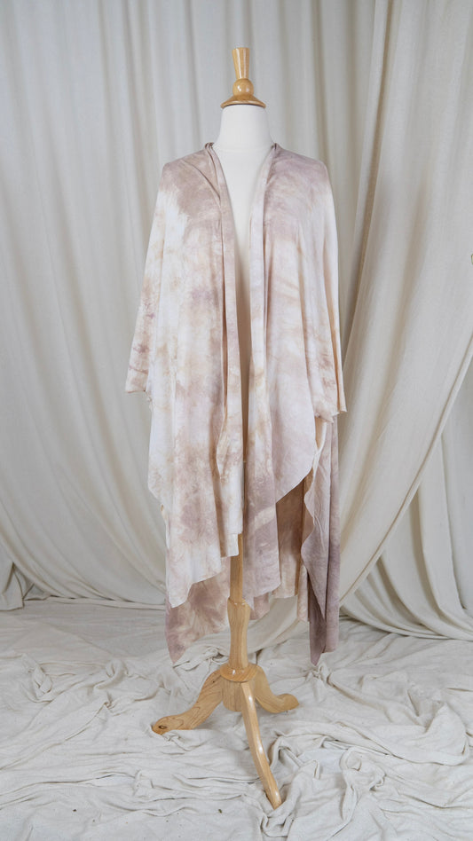 One light pink and white shawl hangs from a bust in front of a white curtain with the front facing the camera.