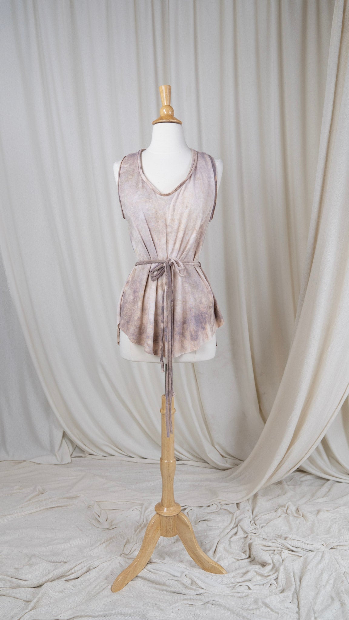 one light rose colored tank top with a scoop neck and a belted waist hangs from a bust with the front facing the camera.