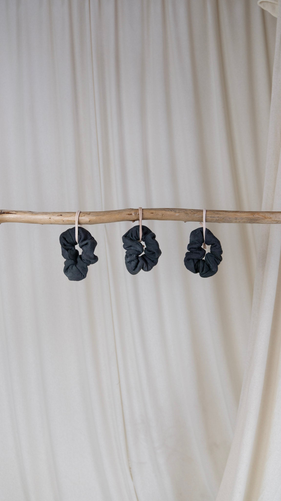 Three dark blue bamboo diamond scrunchies hanging on a piece of driftwood