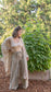 Woman standing in front of plants in a garden wearing raw silk wrap pants, a yellow leotard, and a tan shawl