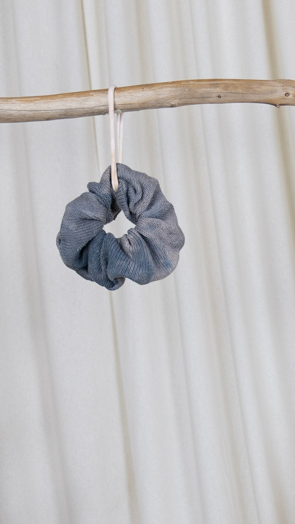 One light purple dyed oversized sweater knit scrunchie hanging from a piece of driftwood