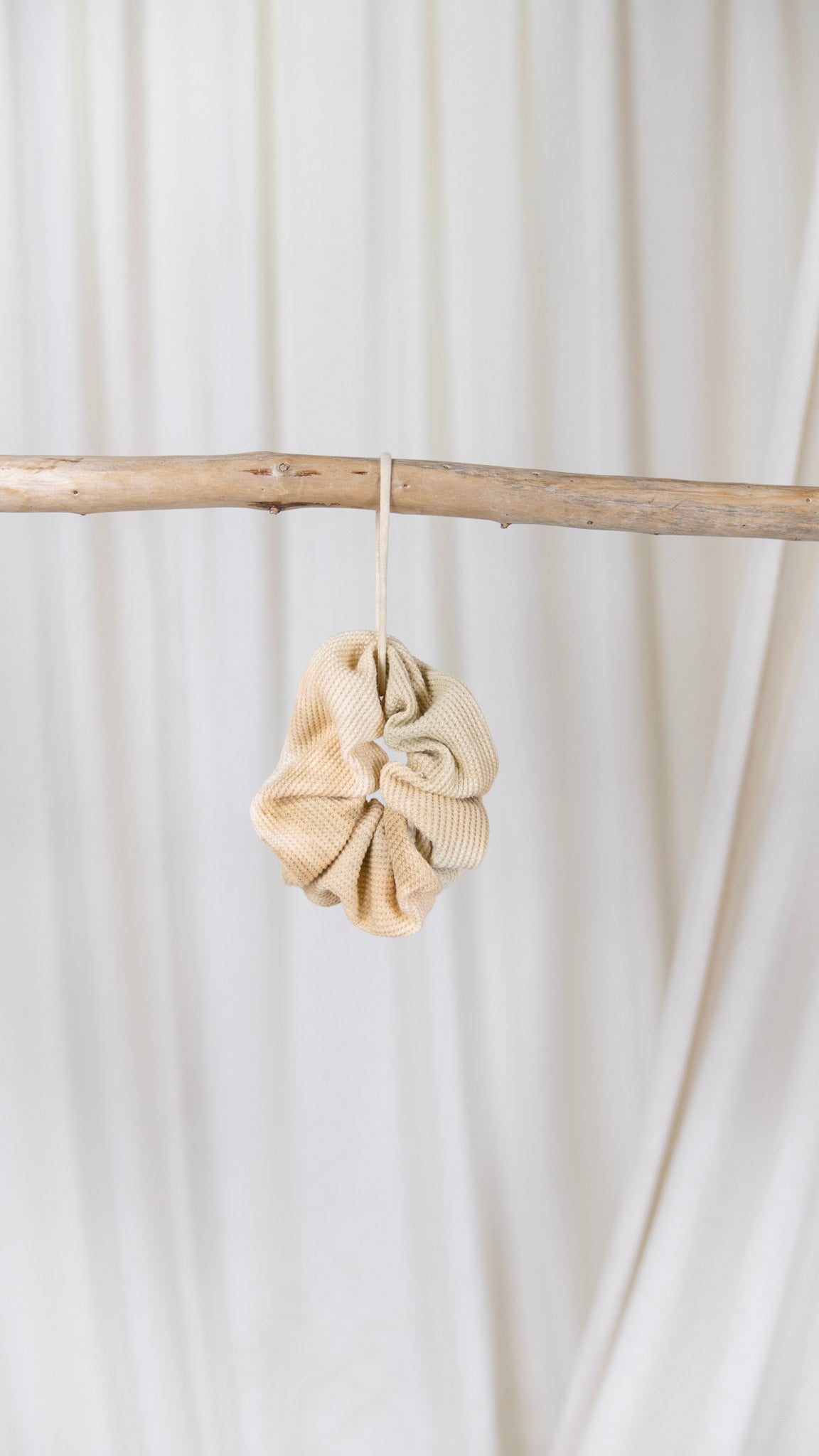 One tan and cream dyed oversized thermal scrunchie hanging from a piece of driftwood