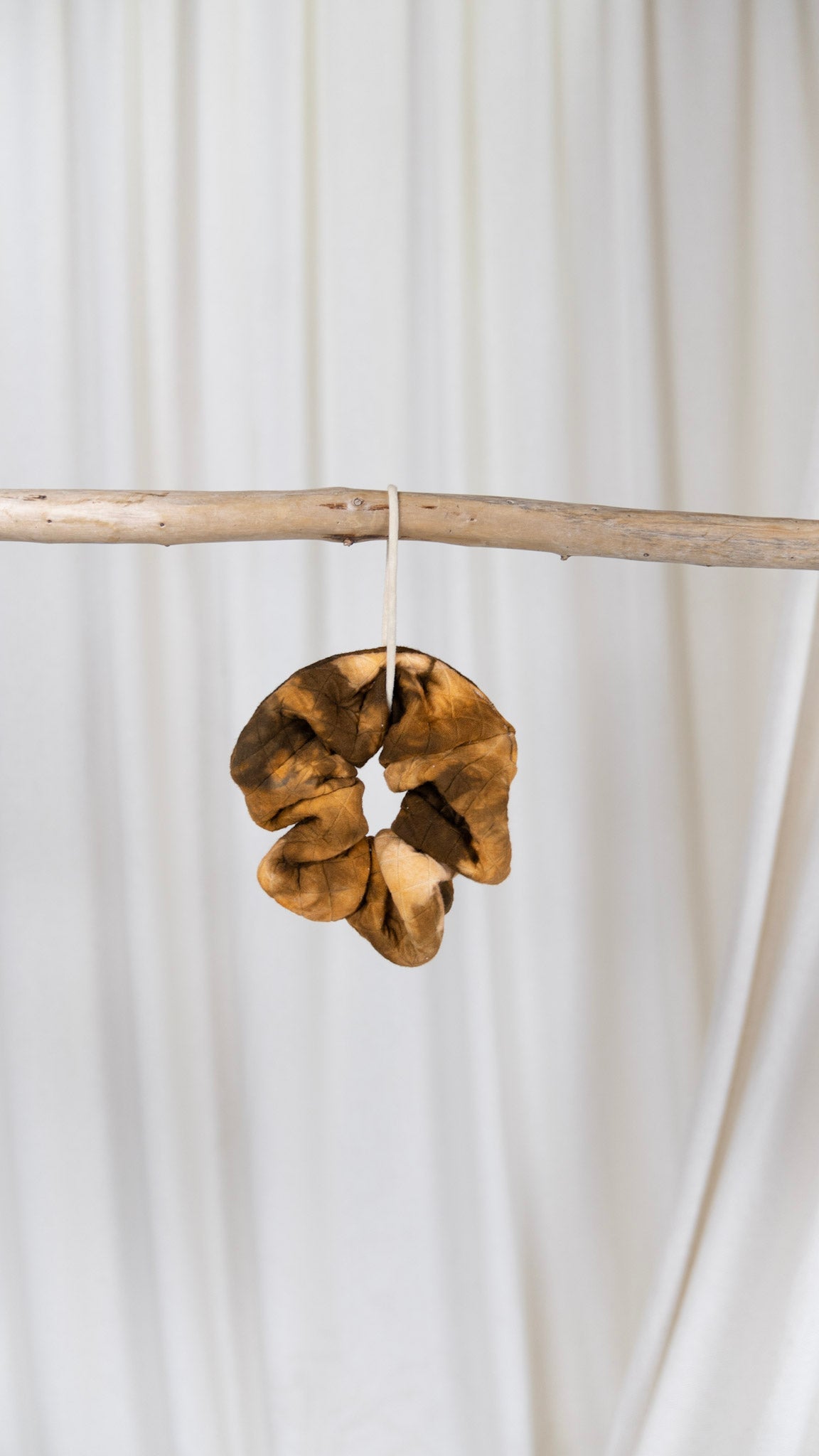 One orange and brown dyed oversized diamond quilted scrunchie hanging from a piece of driftwood