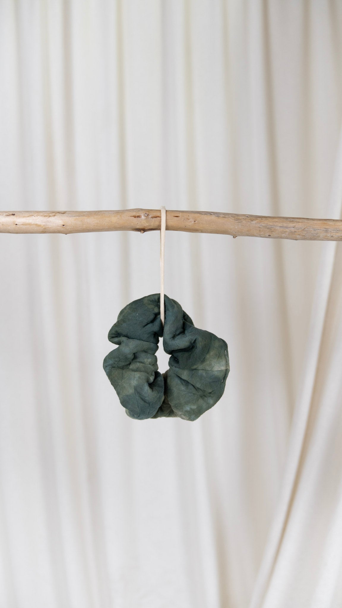 One green dyed oversized diamond quilted scrunchie hanging from a piece of driftwood