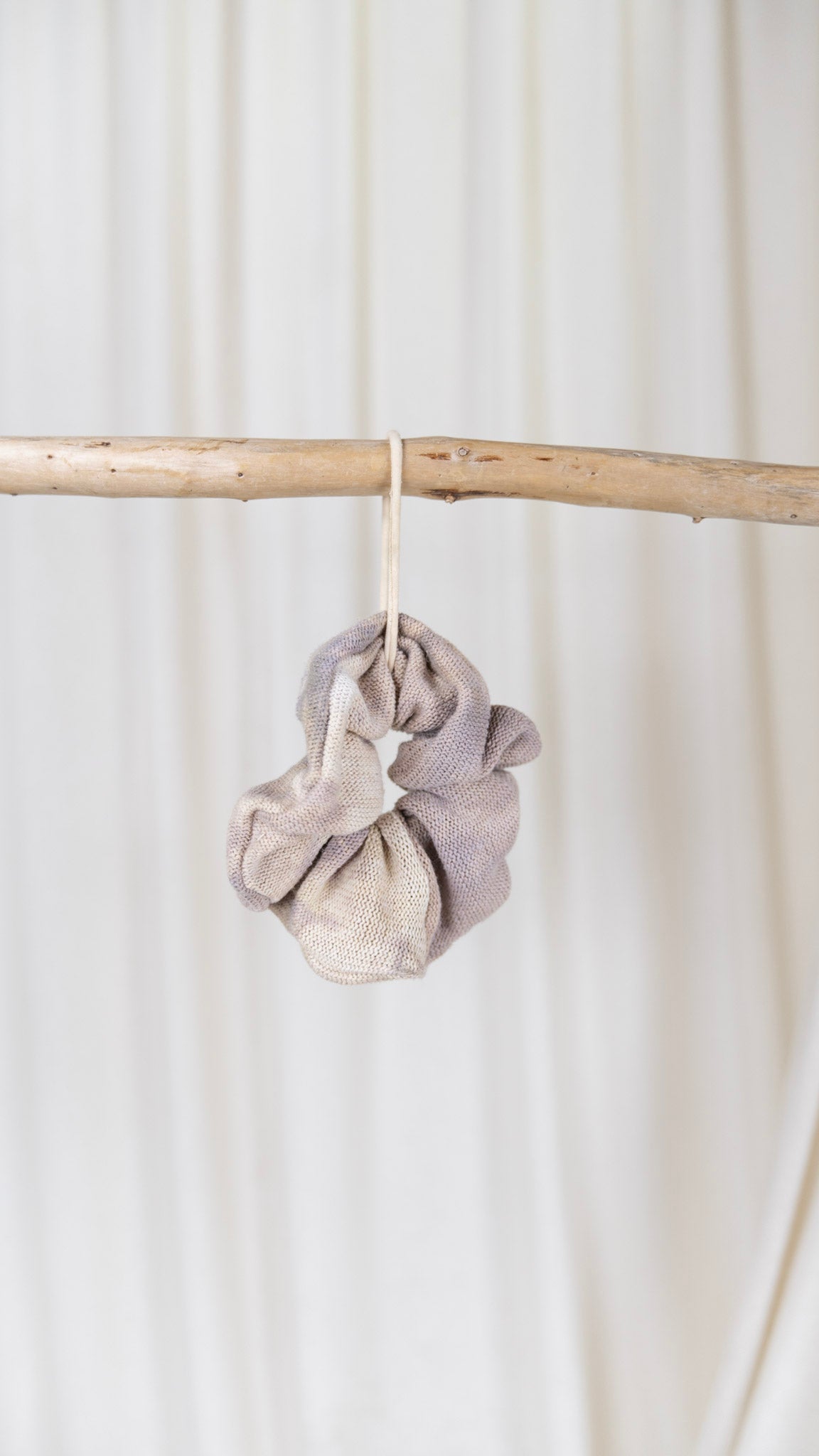 One light purple and cream dyed oversized sweater knit scrunchie hanging from a piece of driftwood