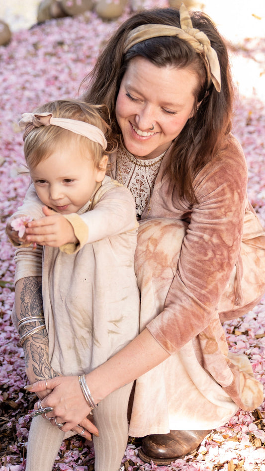 A woman crouching down behind her daughter who is holding fallen cherry blossom petals in her hands