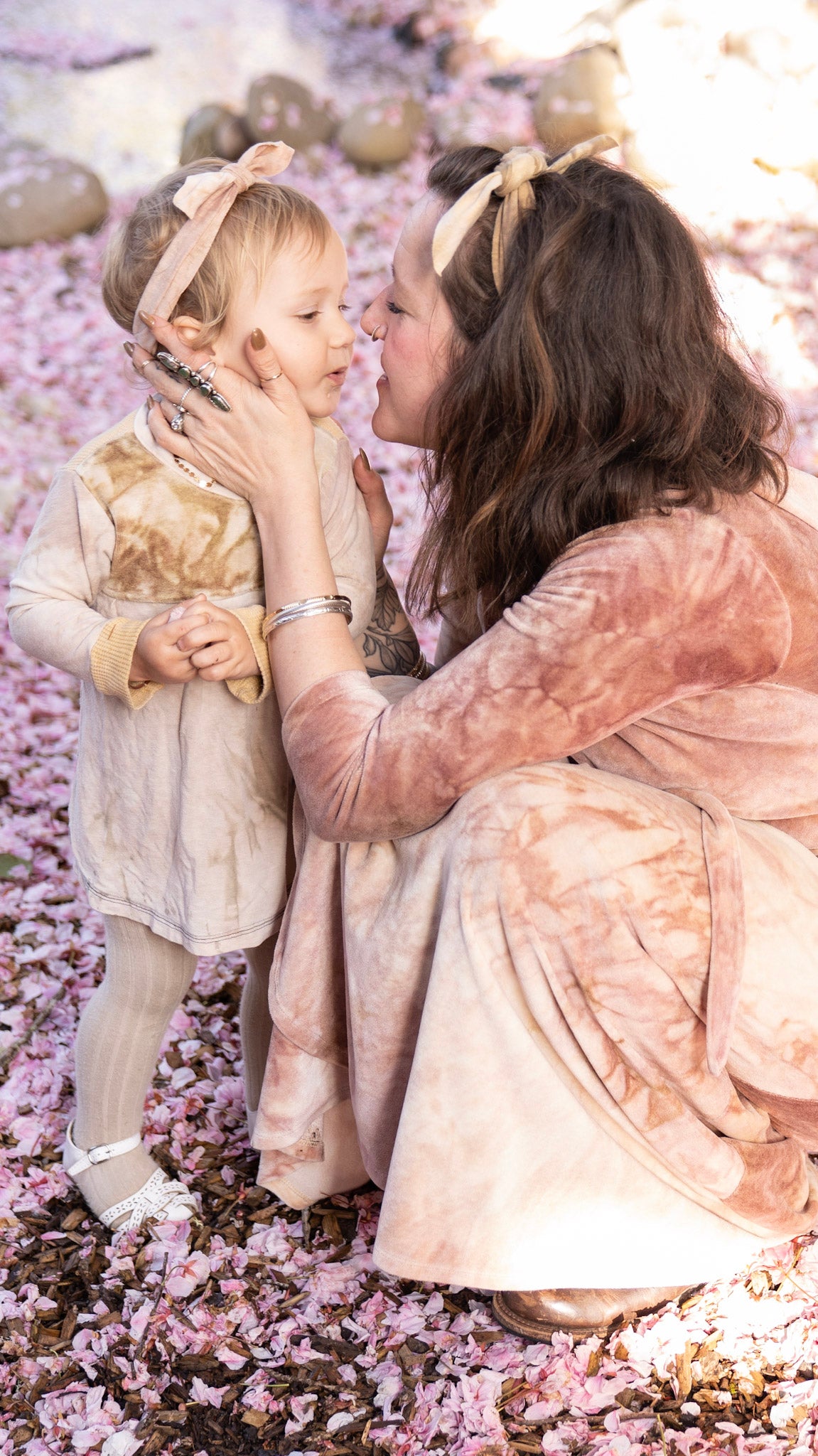 A woman crouched down in a pink velour dress with hands on her daughter's cheeks