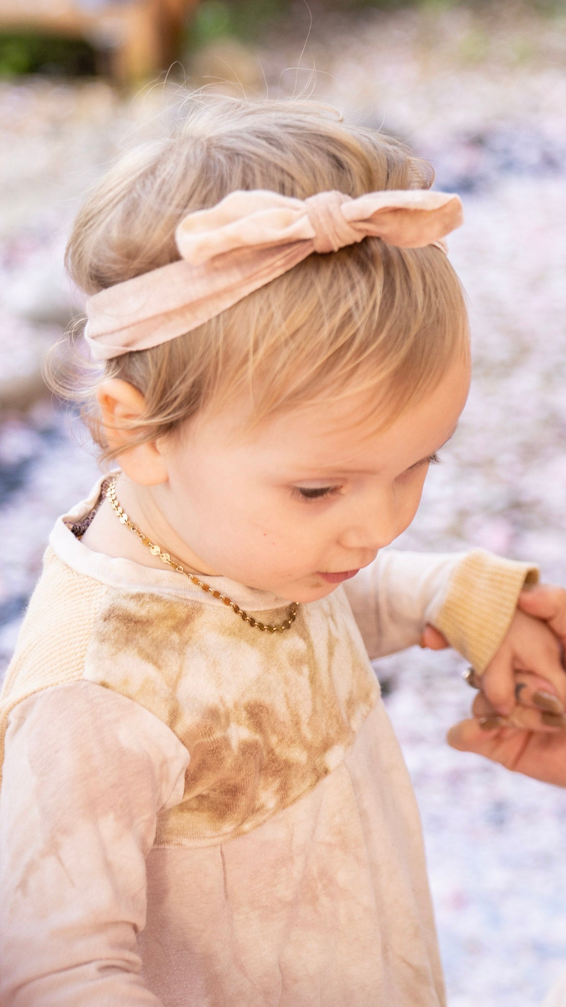 Closeup of little girl standing on the ground surrounded by fallen cherry petals wearing a velour shirt and a light pink hair tie