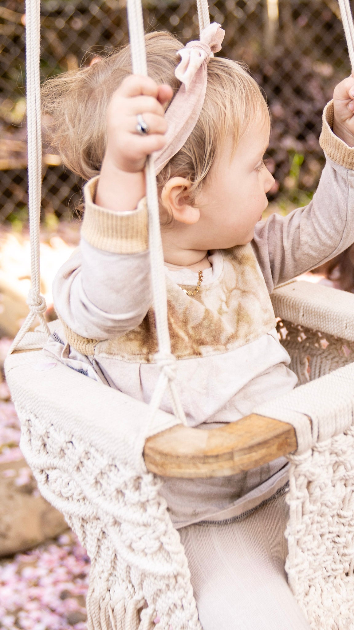 Closeup of a little girl in a macrame swing wearing a velour top and a light pink tie headband