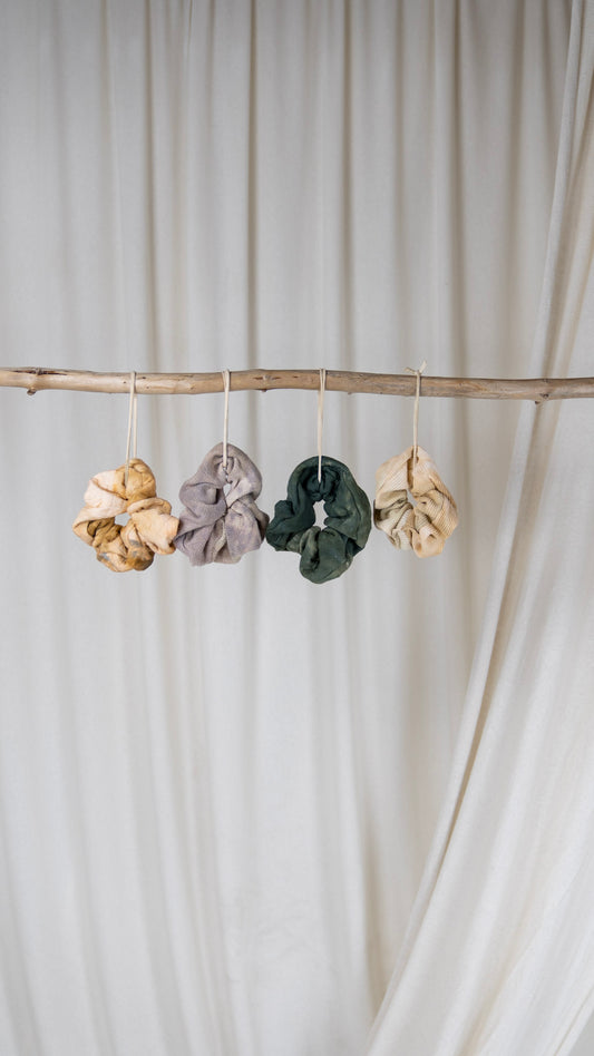 Several oversized scrunchies in various hues and fabrics hanging from a piece of driftwood